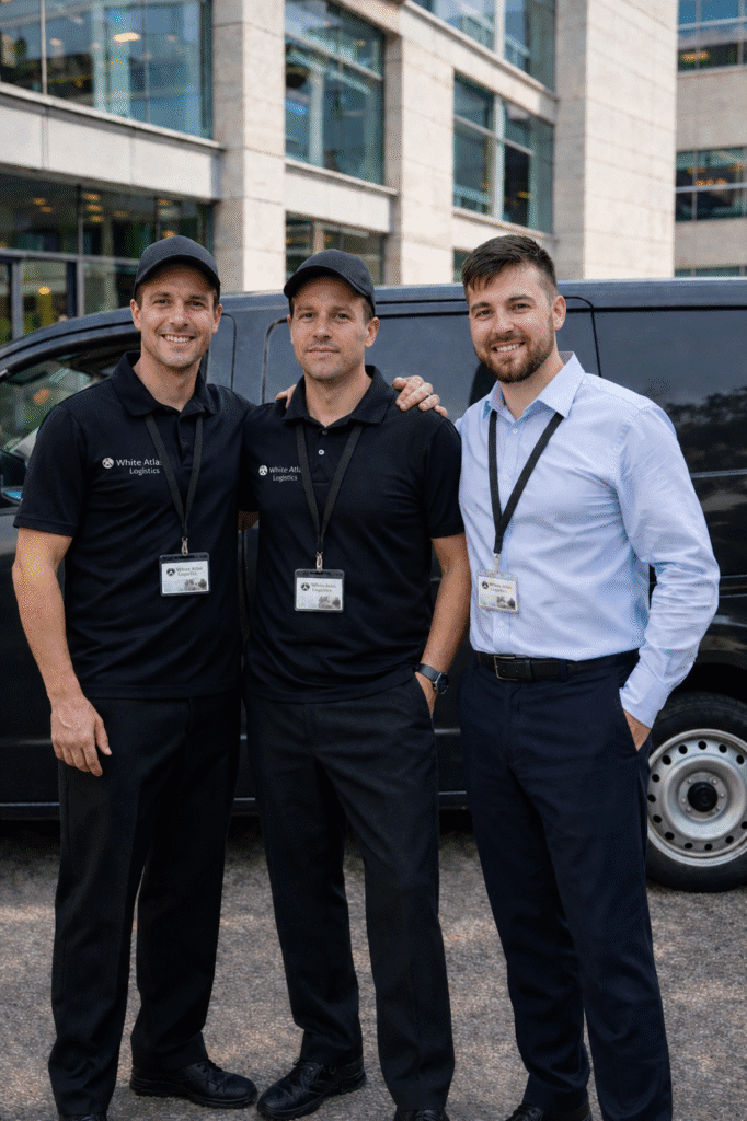White Atlas Logistics team with professional courier drivers and office staff standing beside a black delivery van outside a UK commercial building